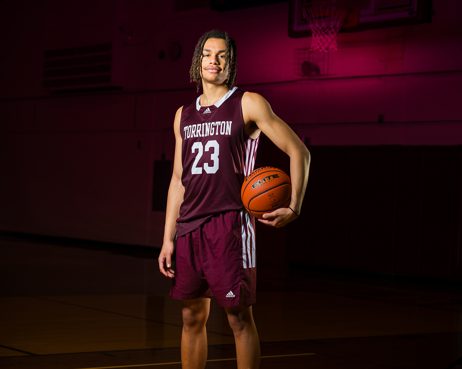 Junior basketball player holds basketball under one arm on a dark court