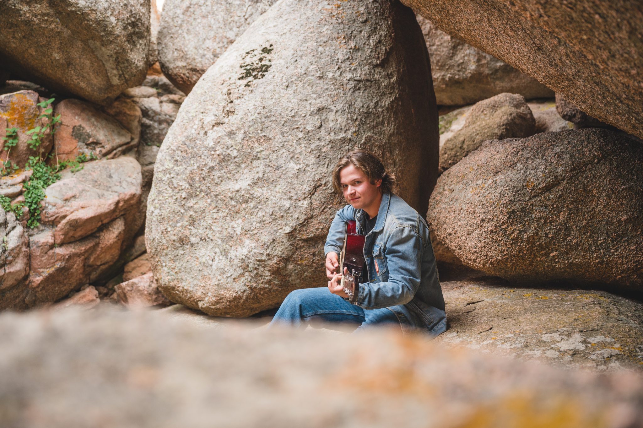 Teen boy playing guitar under overhang of boulders in Vedawoo Recreation Area