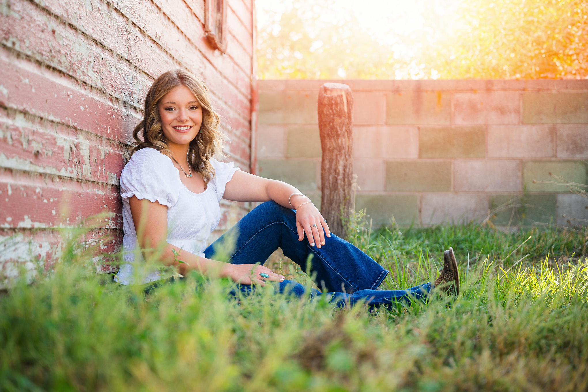 High school senior girl in cowboy boots poses next to red barn