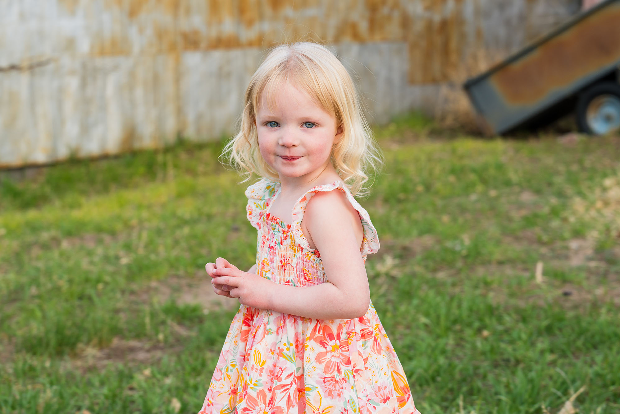 Blond toddler with green eyes poses in an orange and white flowery dress.